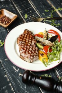 A thick steak searing in a hot skillet beside tongs, seasoning, and a digital thermometer.